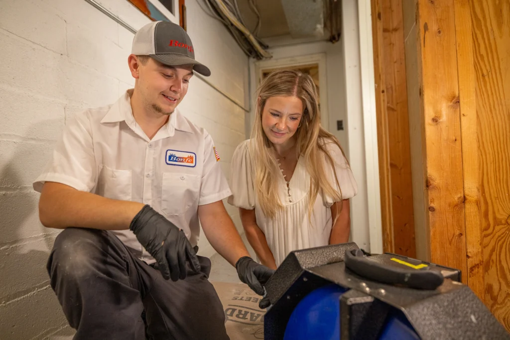The image shows A man and a woman looking at a sewer camera. One, wearing a hat, is explaining what he sees on the camera to the other, who listens to what he is saying.